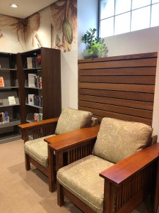 Image of two wooden armed easy chairs with green upholstery next to a book case